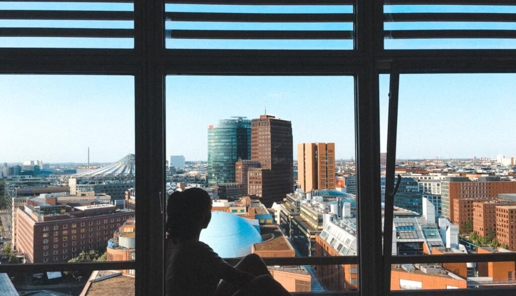 Mujer sentada sola mirando el paisaje urbano de una ciudad desconocida, símbolo del duelo migratorio